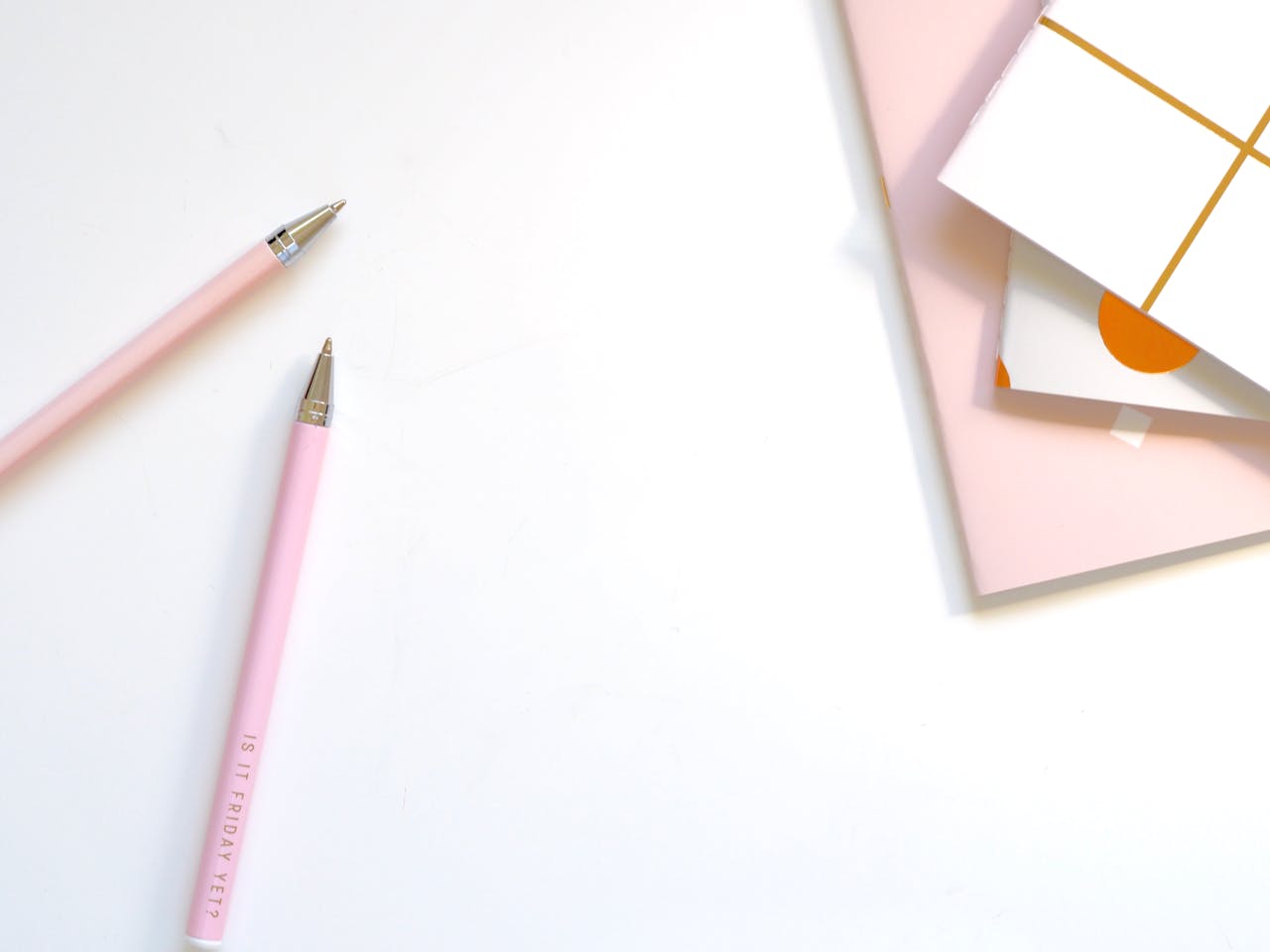 heros-img A minimalist flat lay of pink pens and pastel notebooks on a smooth white background, ideal for office and school themes.